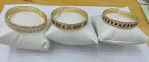 Golden open bracelets with colorful rectangular zircons on white jewelry pillows