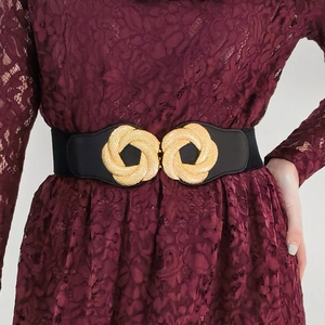 Detailed view of elastic waist belt with large gold textured twist buckle on a dress