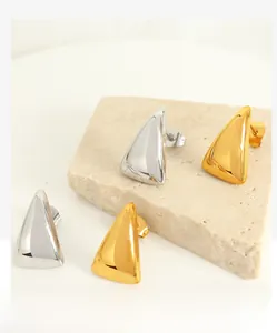 Polished gold and silver triangle stud earrings displayed on textured beige stone