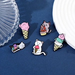Detailed view of five cartoon cat and ice cream enamel pins on a blue fabric background