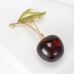 Cute cherry brooch with deep red fruits and green enamel leaf on a white background