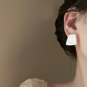 Detail of white geometric resin earring with pearlescent texture worn by a model