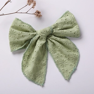 Close-up of light green cotton bow clip with fine floral embroidery and eyelet details