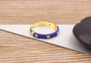 Detail of 18K gold-plated ring with navy blue enamel and zircon inlay on wood background