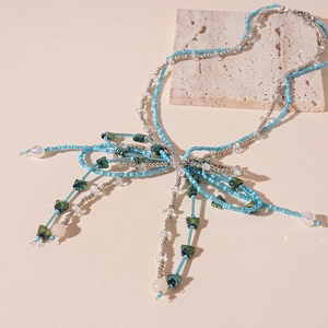 Detail of blue and silver beaded bow necklace with faux pearls on stone texture