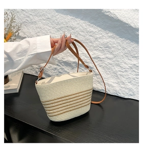 Detail of striped straw bucket bag with brown leather strap on a textured surface