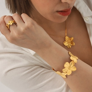Detail of gold floral jewelry set featuring a necklace, ring and bracelet on model