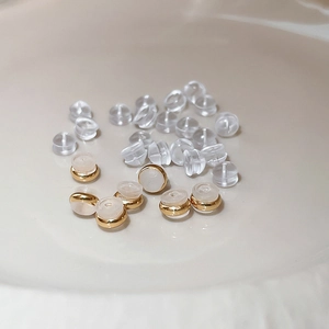 Macro shot of clear plastic bullet and gold-plated ring earring backs on a plate