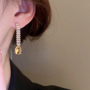 Détail de boucles d'oreilles goutte en cristal jaune et or portées par un mannequin