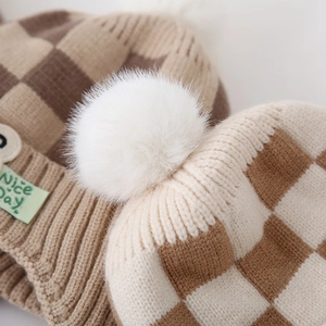 Detailopname van de gebreide ruitjesmuts met witte pompon en Nice Day stoffen label