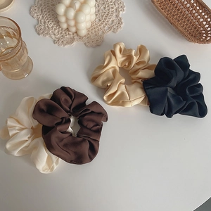 Flat lay of satin scrunchies in cream and brown next to a candle and glass