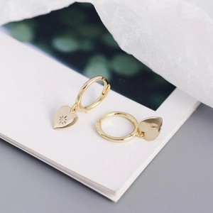 Detail of gold heart earrings with starburst engraving and small zircon crystal