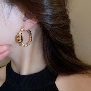 Macro shot of gold hoop earring with pearls and CD logo emblem worn by a model
