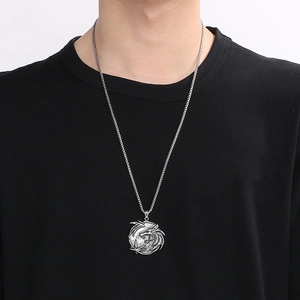 Détail d'un collier pendentif dragon argenté porté sur un pull noir pour homme