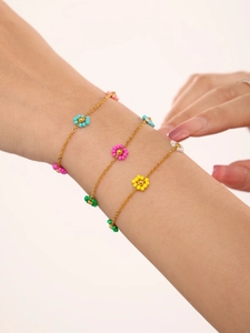 Detail of three layered gold chains with colorful beaded flower charms on model wrist