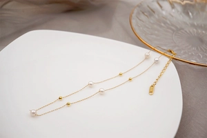 Detailed close-up of golden necklace with freshwater pearls and beads on white plate