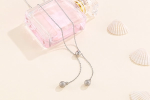 Detail of silver Y-shaped stainless steel necklace draped on a pink perfume bottle