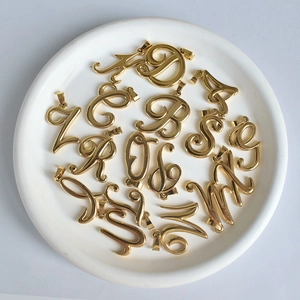 Pendentifs alphabet en acier inoxydable plaqué or 18 carats sur une assiette blanche