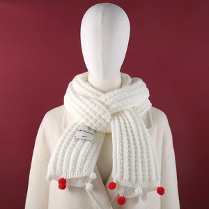 Detail of white knitted scarf with festive red pom-poms and handmade fabric label