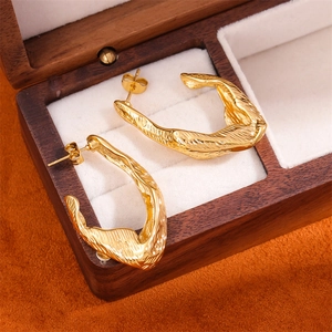 Detailed close-up of golden irregular textured earrings in a premium wooden gift box