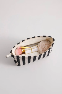 Detail of striped canvas makeup bag with zipper showing brushes, lipstick and hand cream