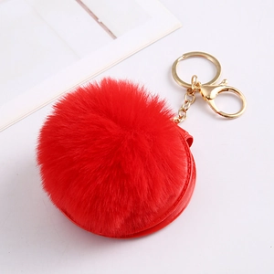 Detail of red faux rabbit fur ball keychain with round leather pouch and golden hardware