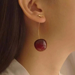 Close-up of long cherry drop earrings with deep red resin fruit on a golden hook