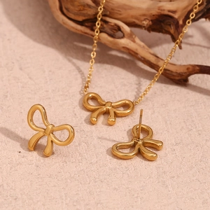 Detail view of gold bow pendant necklace and stud earrings set on a stone background