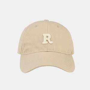Dettaglio del cappellino beige con ricamo 3D della lettera R bianca e tessuto in twill di cotone