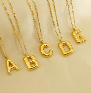 Macro shot of 3D balloon-style A-E initial pendants in polished gold stainless steel