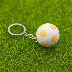 Macro d'un porte-clés mini ballon de football jaune et blanc sur fond d'herbe verte