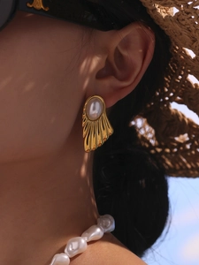 Detail of vintage gold fan-shaped stud earrings with pearls on a model in a resort setting