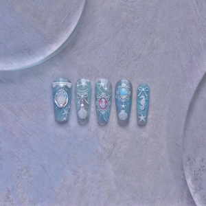 Detail of blue press-on nails featuring embossed seahorse, shell, and pearl ocean motifs