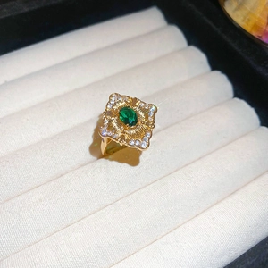 Close-up of vintage gold ring with emerald green stone and white zircon floral details