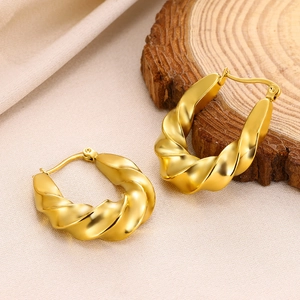 Close-up of golden hollow twisted spiral hoop earrings on natural wooden surface