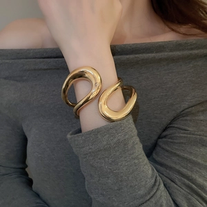 Detail of a polished gold irregular geometric cutout cuff bracelet on a model's wrist
