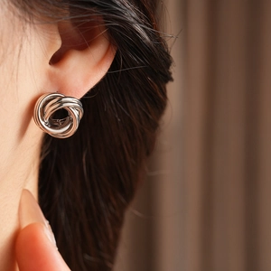 Gros plan de boucles d'oreilles nœud argentées portées montrant une texture métallique