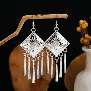 Detailed view of silver ethnic leaf tassel earrings hanging on a natural wooden branch