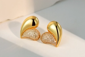 Detailed close-up of heart studs with pavé zircon and polished gold finish on stone display