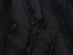 Close-up macro of black tweed fabric texture featuring frayed fringe details for winter coats