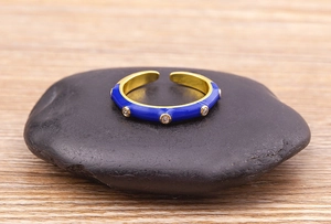 Detail of gold-plated ring featuring blue enamel and sparkling zircons on a black stone