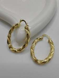 Close-up of golden twisted texture hoop earrings on a white ceramic display tray