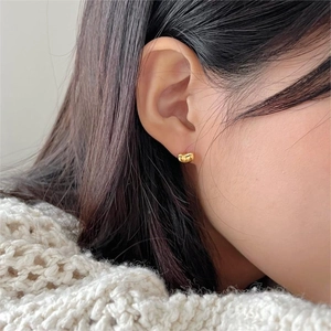 Close-up of small golden bean stud earring worn by model against a white knit sweater