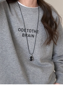 Detail of a minimalist black gourd resin pendant necklace worn on a gray sweater