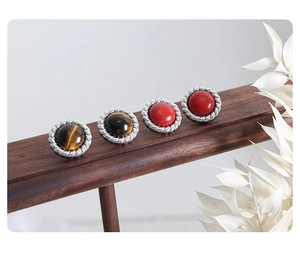 Detailed view of silver finish stud earrings with tiger eye and red agate on wooden stand