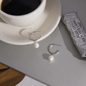 Detailed view of silver C-shaped hoop earrings with white freshwater pearl pendants