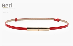 Detail of skinny red patent leather belt with a slim polished gold rectangular buckle
