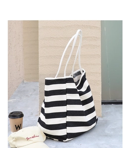 Detail of a striped canvas tote bag with cotton rope handles in a minimalist outdoor setting