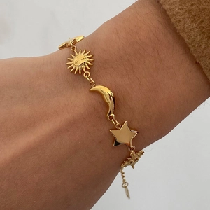 Detail of gold-plated bracelet featuring sun moon and star charms worn on wrist