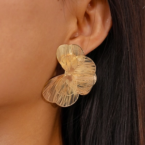 Detailed view of large gold layered flower petal earrings with intricate hollow textures